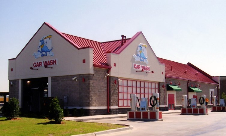 Brick building with a red roof has sign that says "CAR WASH" with blue kangaroo logo on two sides of the building. Vacuuming stations sit outside.