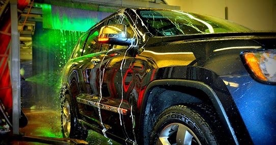 Black SUV goes through Splash Car Wash. Soap drains down the side of the vehicle.