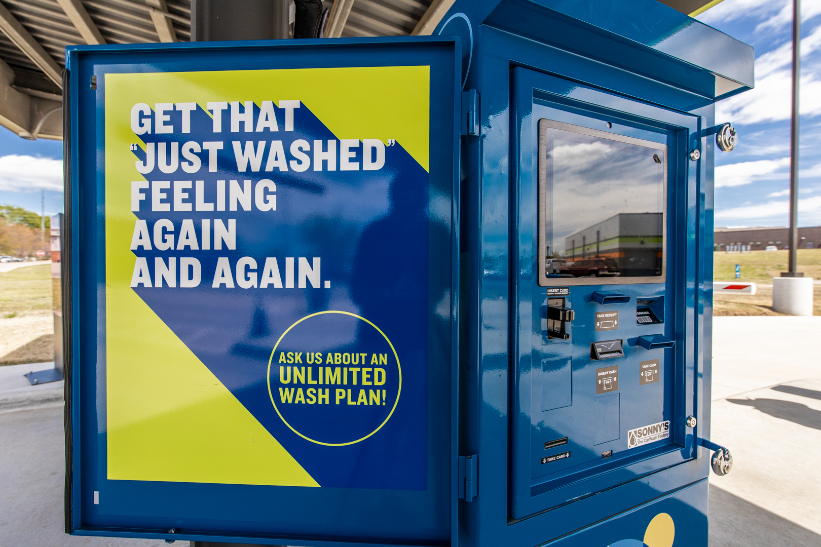Blue Splash Car Wash payment kiosk with sign saying "GET THAT 'JUST WASHED' FEELING AGAIN AND AGAIN. ASK US ABOUT AN UNLIMITED WASH PLAN!"