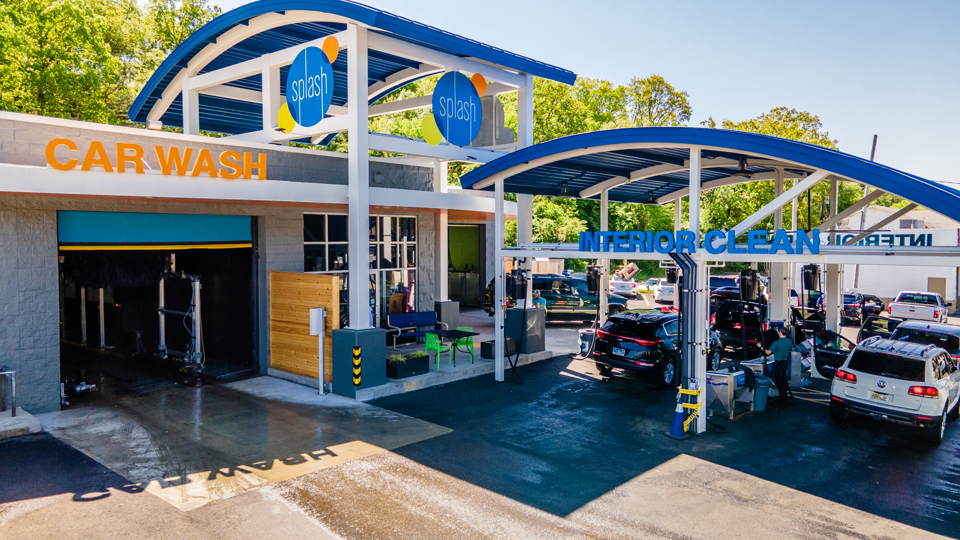 Exterior of Splash Car Wash building with "CAR WASH" and "INTERIOR CLEAN" stations. Cars are in line under the "INTERIOR CLEAN" sign under a blue pavillion.