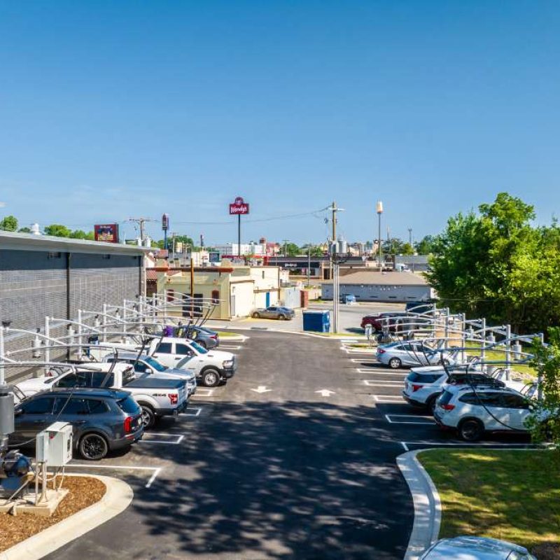 Vacuuming stations are spaced across an entire Splash Car Wash parking lot, half facing the building and the other half facing a wooded area. Vehicles are parked at the majority of the vacuuming stations.