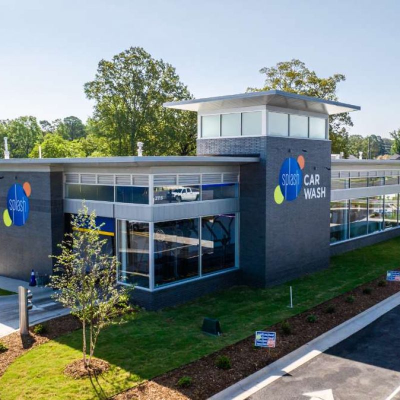Front and side of Bryant Splash Car Wash building are shown. Both sides have gray section of walls with the Splash logo next to windows. A manicured grassy area surrounds the side of the building.