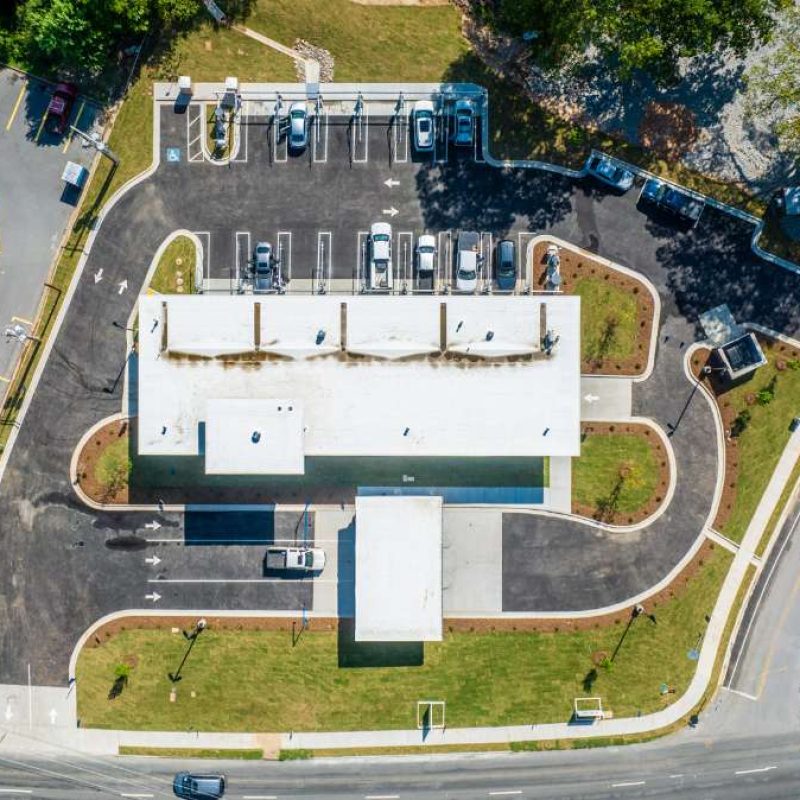 Direct overhead picture of Bryant Splash Car Wash, surrounded by cars in parking lots with vacuuming stations. White arrows on the asphalt direct drivers on where to go.