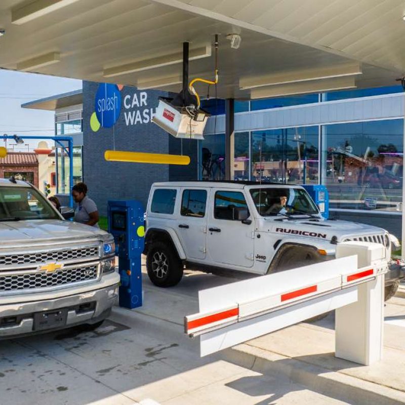 White Jeep and silver truck check into the Bryant Splash Car Wash. A female Splash employee stands at the driver's side window of the silver truck, speaking with the driver.