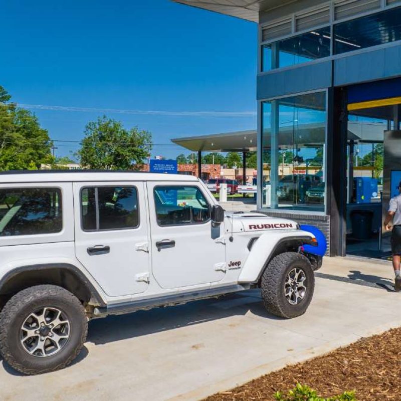 A Splash Car Wash employee walks outside in front of the car wash entrance. A white Jeep waits to pull into the car wash.