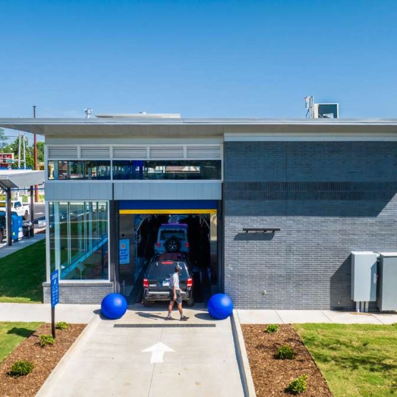 A white arrow points to the entrance for the Splash Car Wash, with cars in line entering the gray building. Cars are on either side of the building: in line to get into the car wash and parked at the outside vacuuming stations.