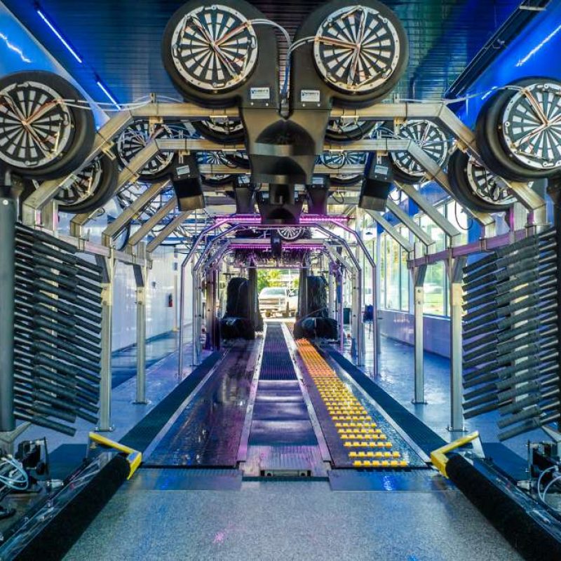 White truck waits outside at the beginning of rollers/tracks to go through the entire Splash Car Wash process, ending at the drying station.