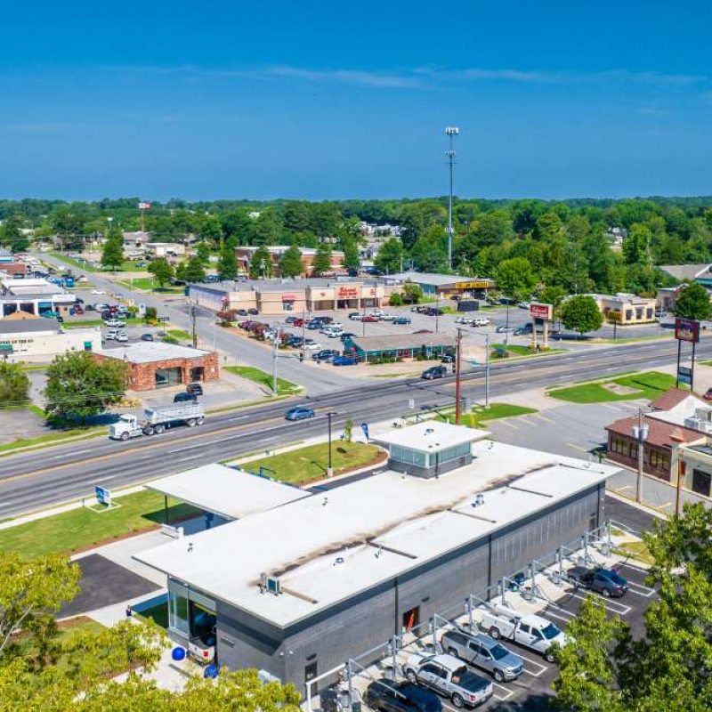 View of top of Bryant Splash Car Wash building with vehicles parked in outside vacuuming stations and cars driving on highway next to the building.