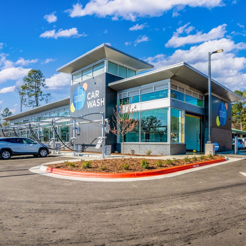 Outside of Sherwood Splash Car Wash facility with cars parked in vacuuming stations next to the building. Windows line the building from front to back.
