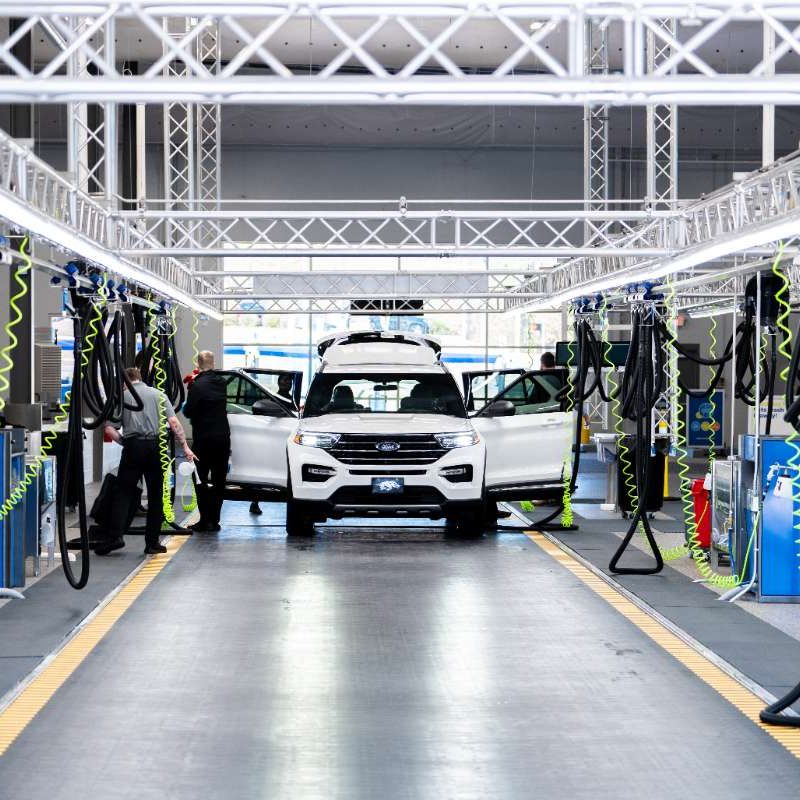 A white vehicle sits in the middle of an indoor Splash Car Wash vacuuming station. All four car doors and truck are open as Splash Car Wash employees clean the inside of the vehicle.