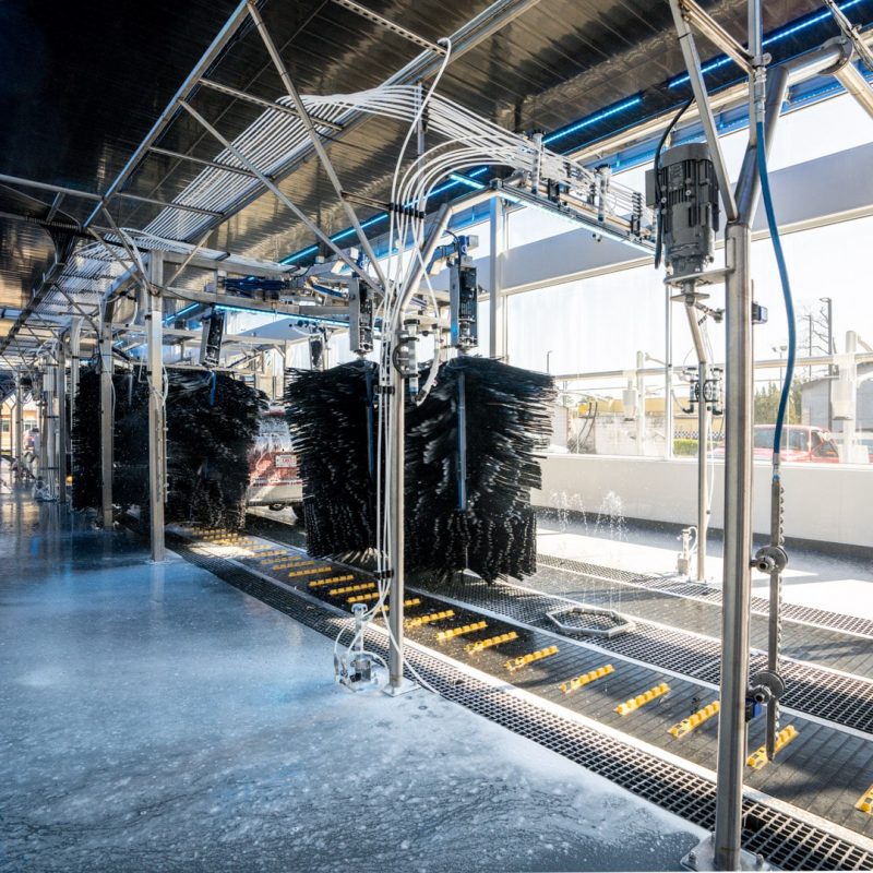 A car is moved through the car wash on the conveyer belt as brushes wipe down the car.