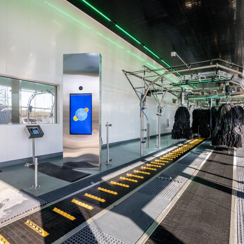 Inside view of Sherwood Splash Car Wash with rollers on the ground to move a vehicle through the stations. A digital sign with the Splash logo sits nexts to the tracks for drivers to see.