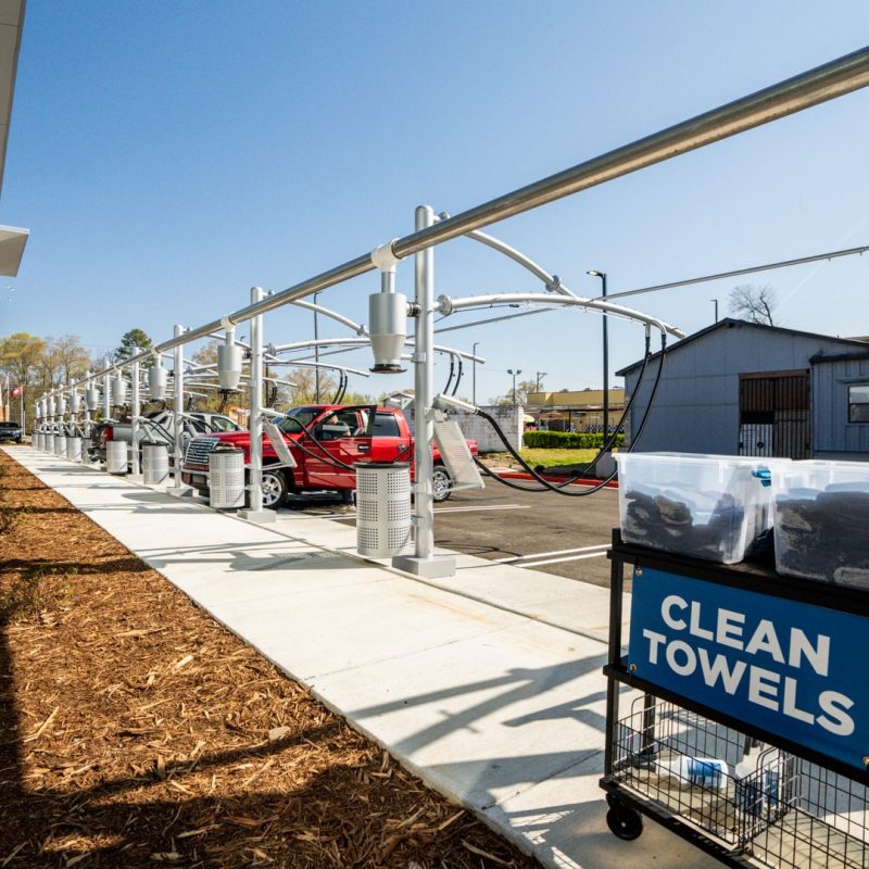 View of back of vacuuming stations. A rack with rollers sits on the sidewalk next to the vacuuming stations. Two buckets with towels stacked inside sit on the rack with a sign saying "CLEAN TOWELS."