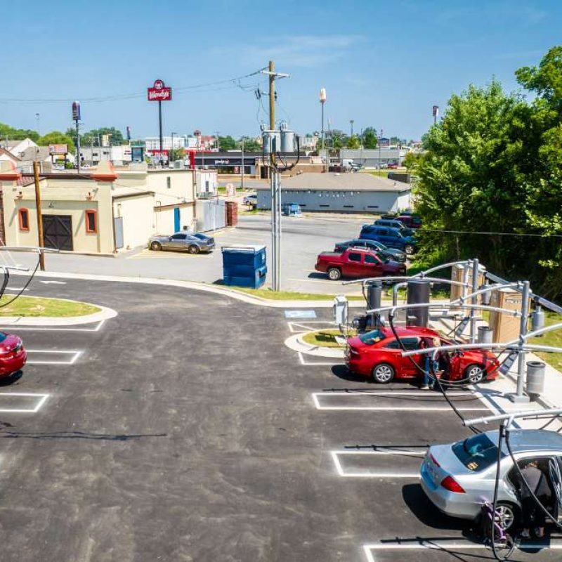 Three cars--two red and one silver--are parked at the outside vacuuming stations. A person at each car has a car door open and is vacuuming the inside of their car.