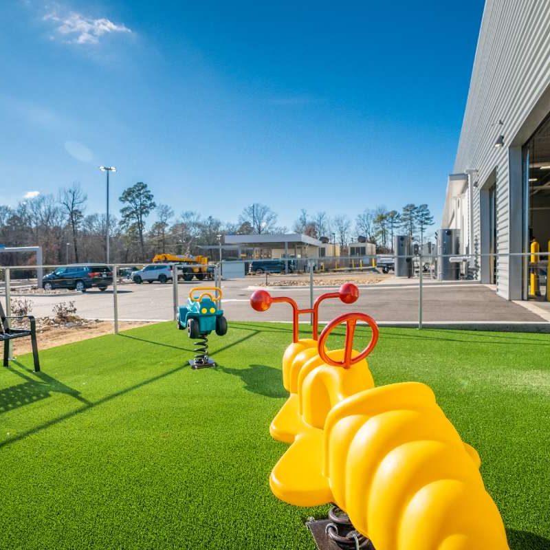 Area outside of Splash Car Wash building with bench, green artificial turf, and two spring rider playground equipment toys stabilized in the ground.